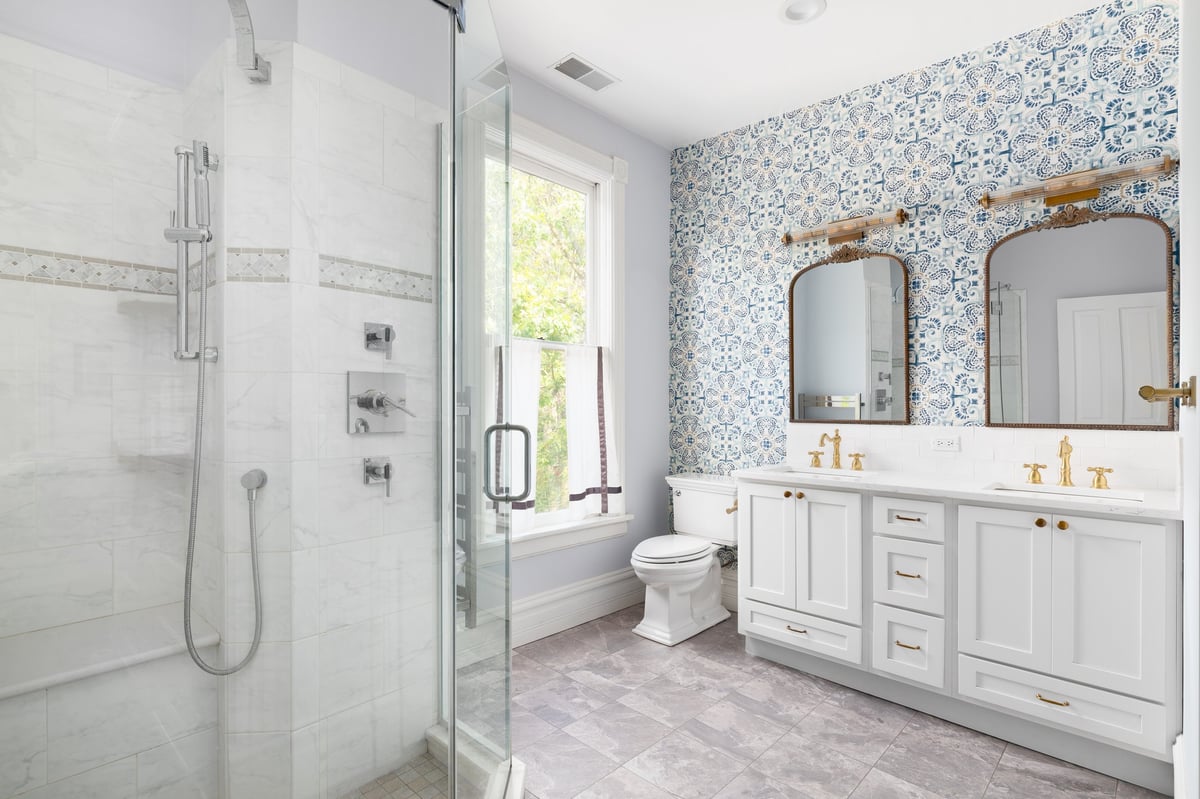 Stylish bathroom with patterned blue wallpaper, tiled walk-in shower, and gold fixtures