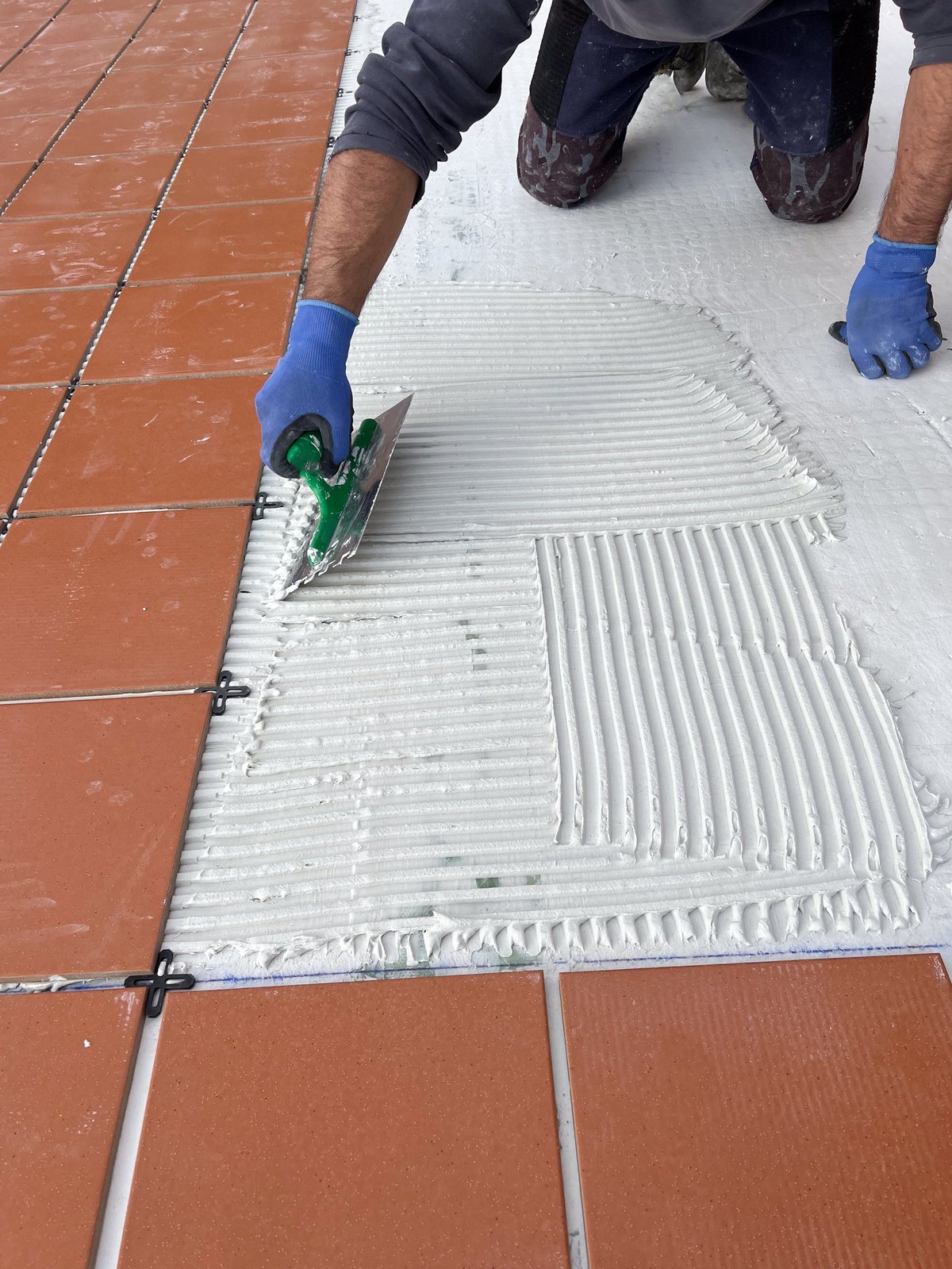 Construction worker spreading tile adhesive on floor using notched trowel preparing surface for tiling