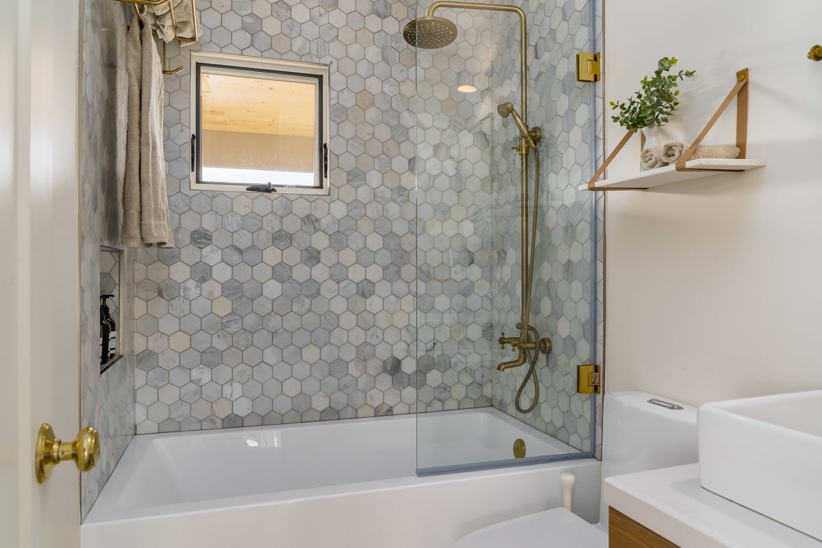 Modern white bathroom with walk-in shower, hexagonal tile, and gold brass fixtures