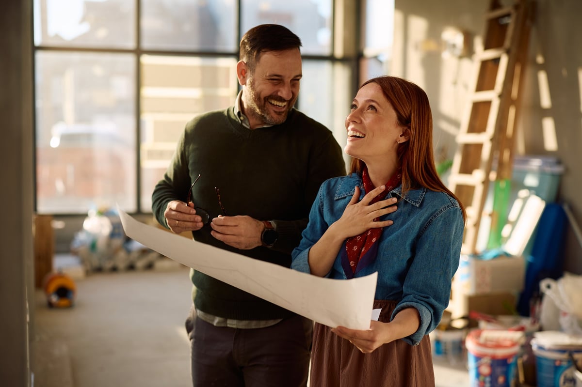 Happy couple laughing while examining blueprints during home remodeling process