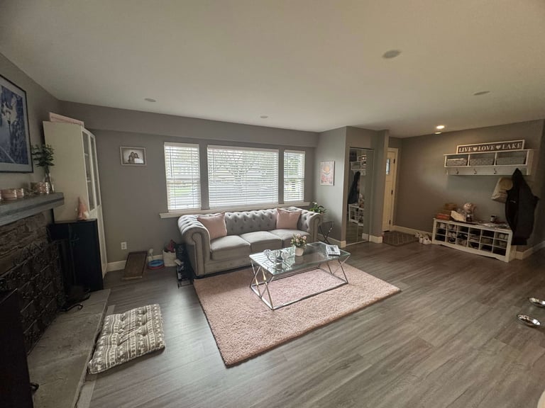 Modern living room with gray walls, gray sofa, coffee table, fireplace, and hardwood flooring, accented with area rugs and natural lighting from large windows