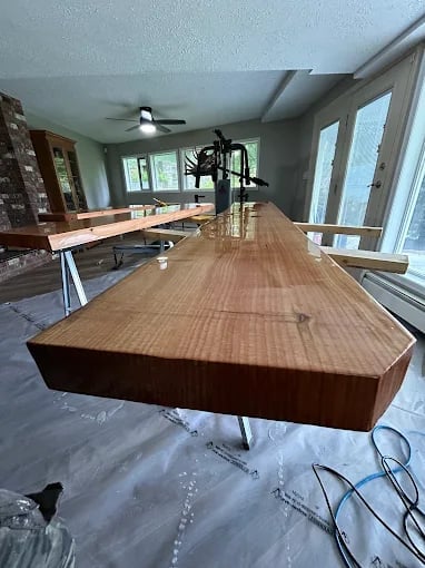 Modern woodworking workshop with curved wooden countertops in progress, featuring bright natural light from large windows and ceiling fans
