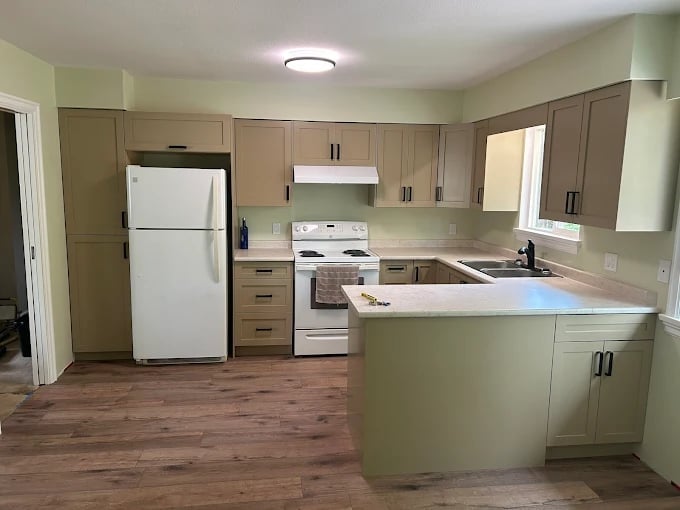 Spacious kitchen with light green cabinets, white appliances, island counter, and wooden flooring