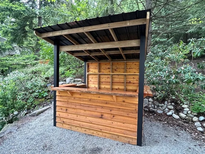 Custom vendor booth and pergola construction by our Chilliwack handyman in garden setting with wooden booth and metal frame