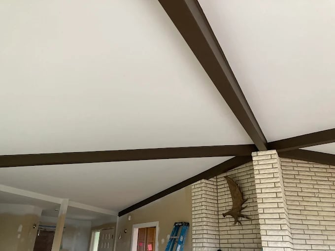 Interior ceiling repair and beam restoration by our Chilliwack handyman featuring dark wooden beam supports and exposed brick